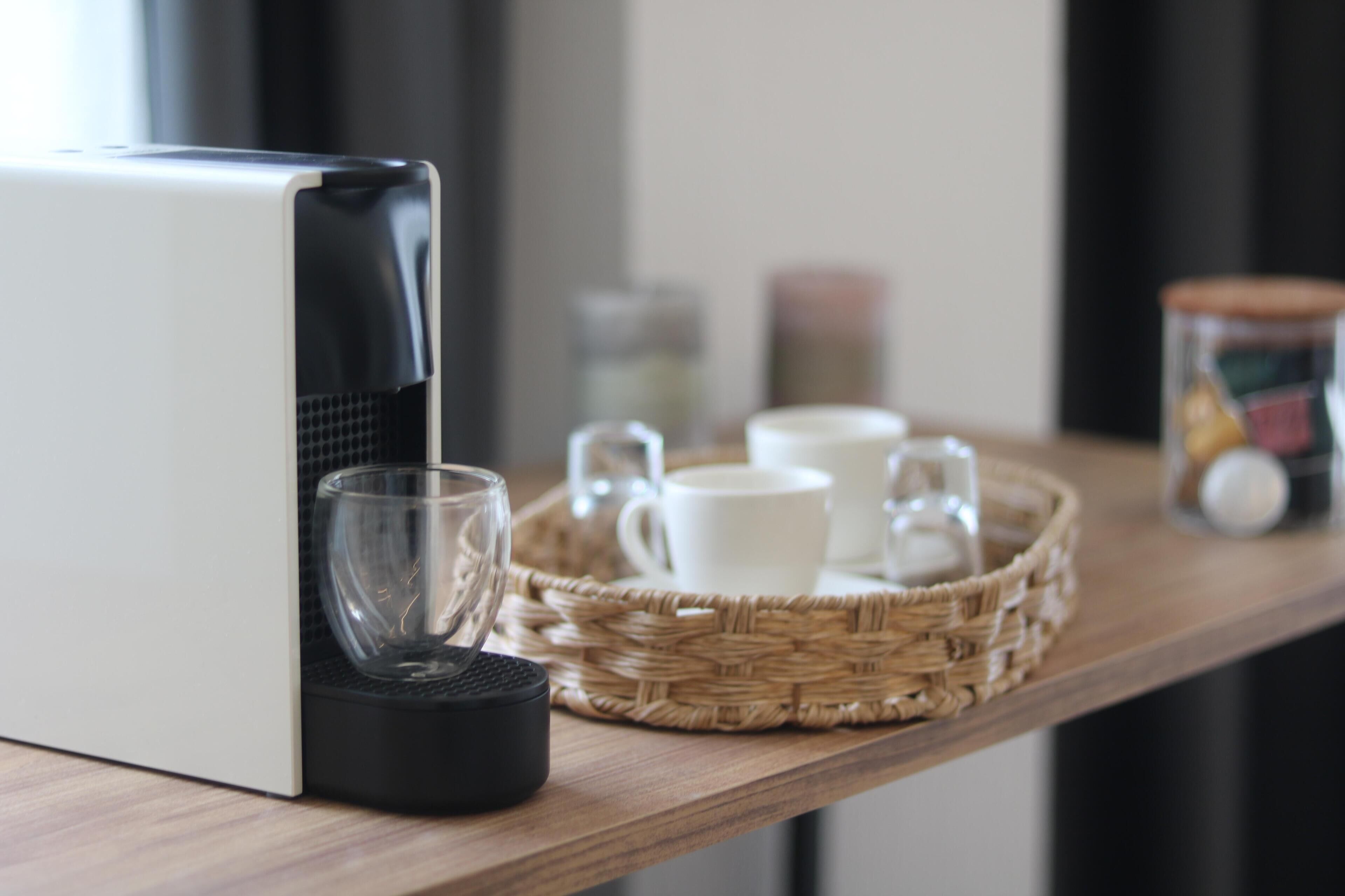 A kitchen counter with a coffee maker, a glass, and a wicker tray holding cups and a jar.