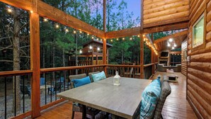 A wooden cabin with a large deck, outdoor seating, and a fireplace. - Luxury Cabin | Hot Tub, Fireplace, Game room (Broken Bow)