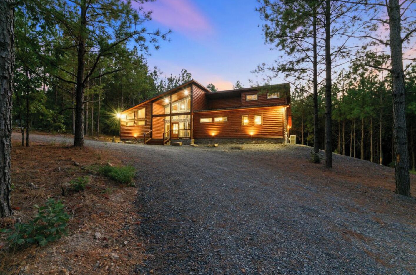 A cabin with a gravel driveway, surrounded by trees.