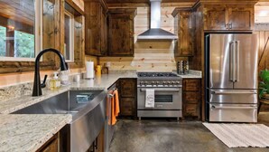 A kitchen with wooden cabinets, a stainless steel refrigerator, a stove, and a sink. - Luxury Cabin | Hot Tub, Fireplace, Game room (Broken Bow)