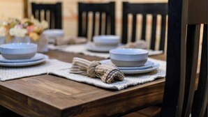 A wooden dining table set with white plates and bowls, a striped napkin, and a woven placemat. - Luxury Cabin | Hot Tub, Fireplace, Game room (Broken Bow)