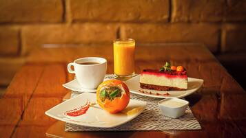 A table with a slice of cheesecake, a cup of coffee, a glass of orange juice, and a small dish of sauce.