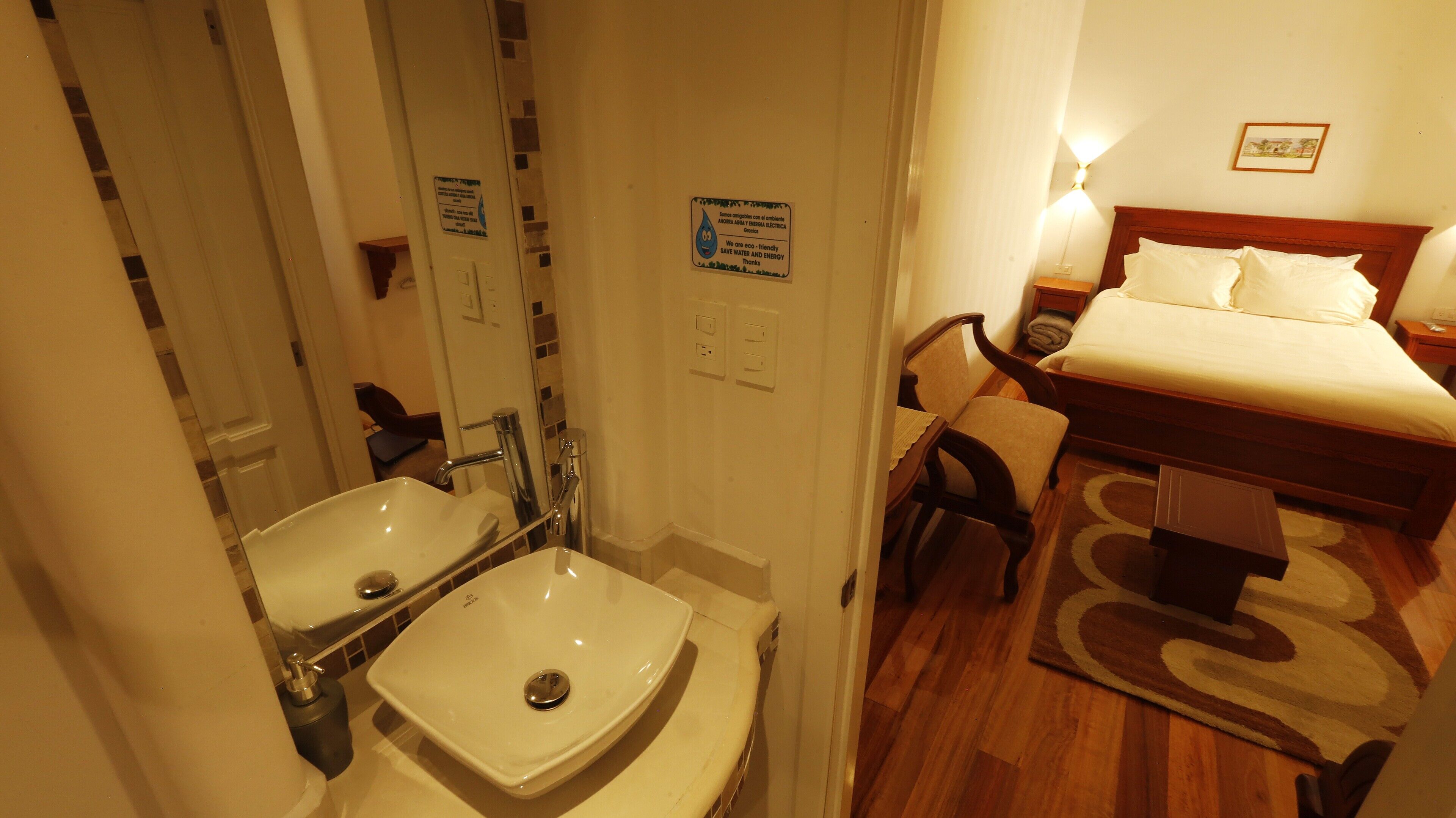 A hotel room with a bed, two sinks, a chair, and a rug.