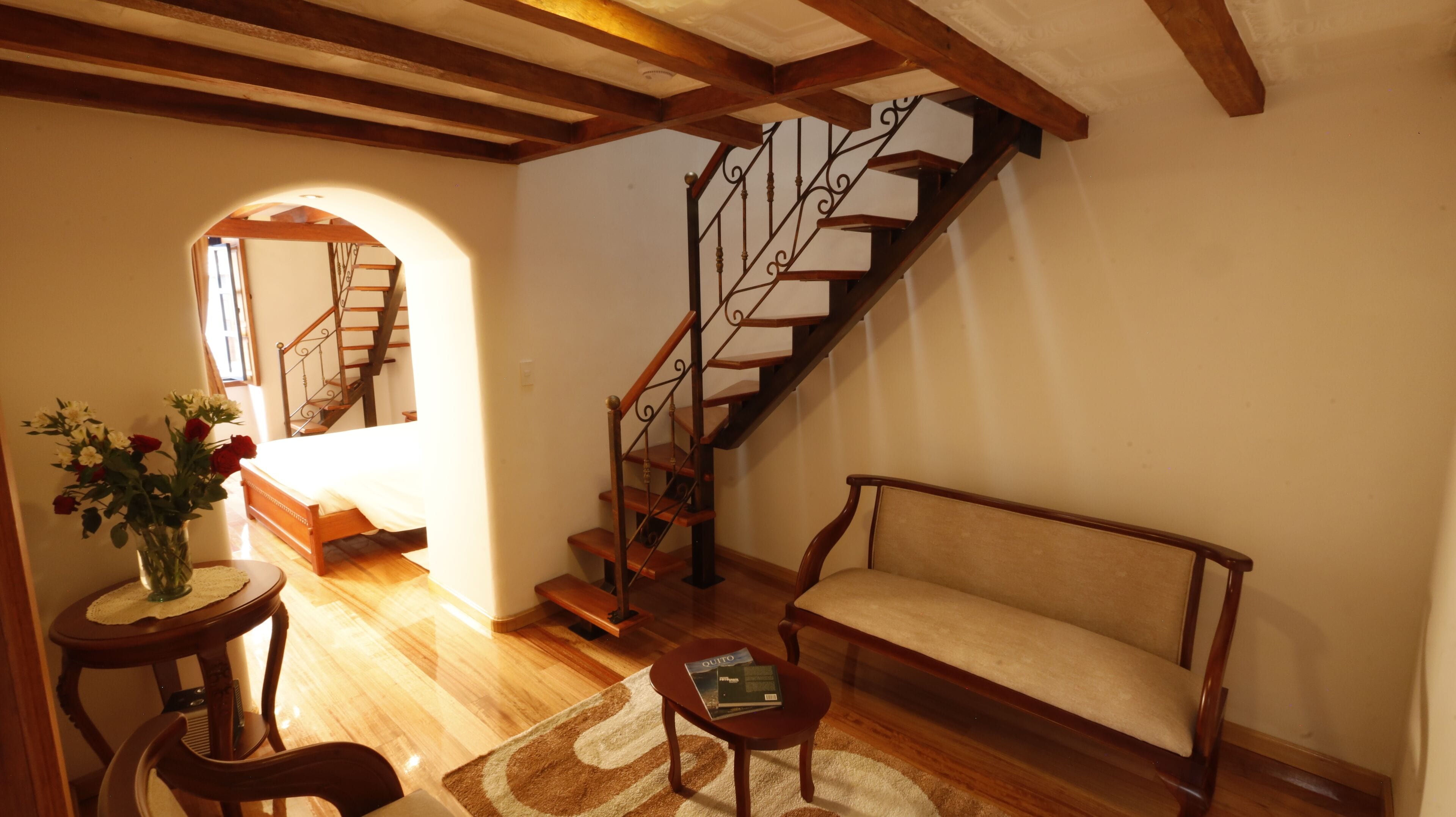 A spacious living room with a wooden staircase, a sofa, a coffee table, and a vase of flowers.