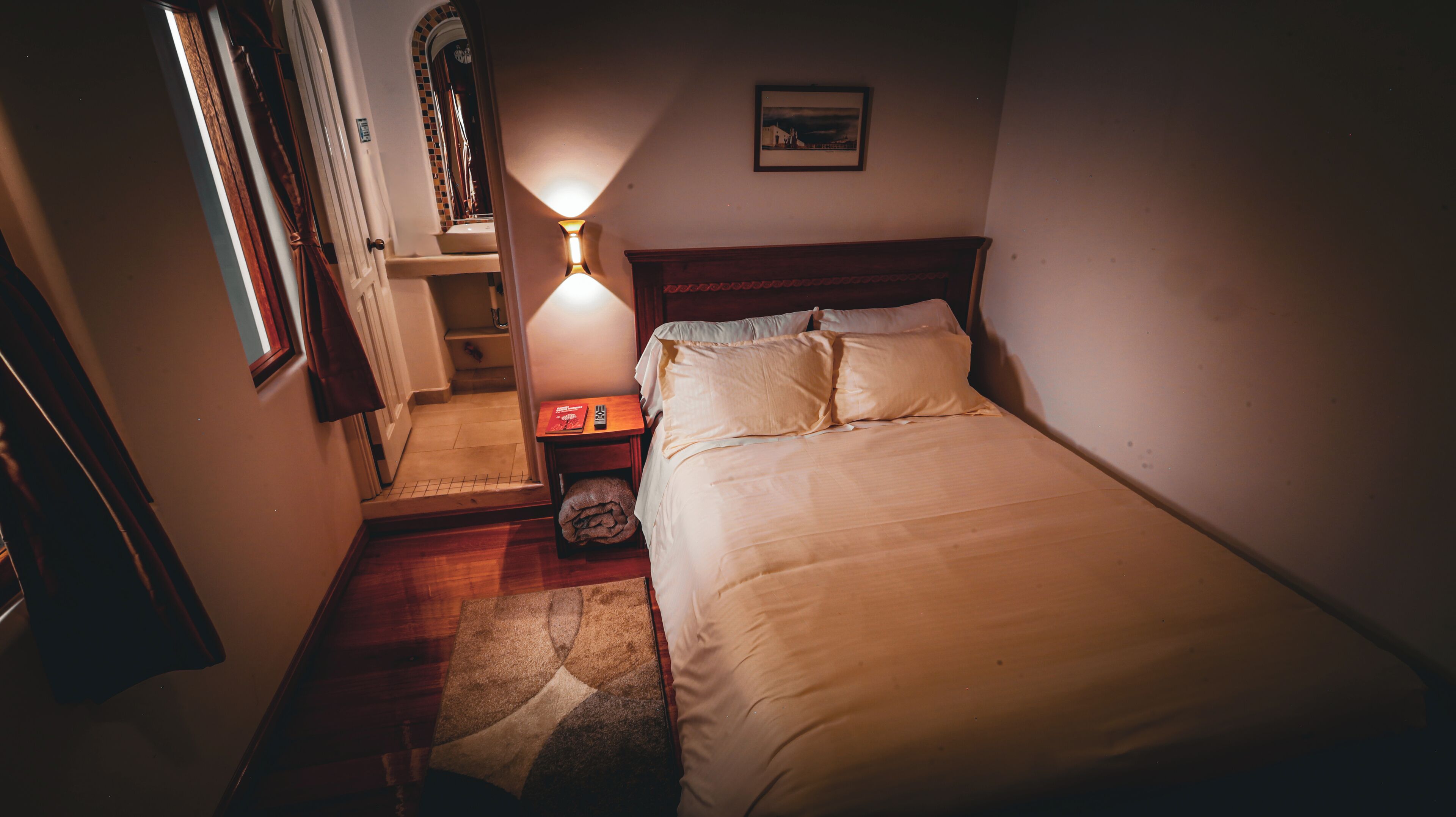 A narrow staircase leading to a bedroom with a bed, a nightstand, a lamp, and a framed picture on the wall.