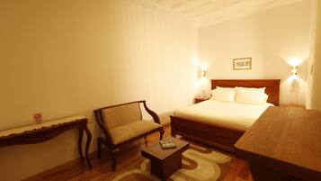A hotel room with a bed, a wooden chair, a small table, and two wall-mounted lamps.