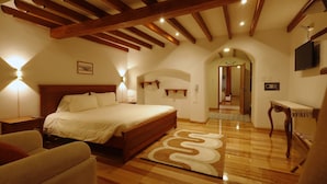 Un dormitorio con una cama de madera, mesitas de noche, un sofá, una alfombra y un televisor montado en la pared.