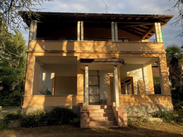 Un edificio de dos pisos con un balcón, una entrada principal y una escalera que conduce a la entrada.