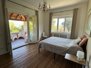 Un dormitorio con cama, mesita de noche, silla, ventana y balcón con sillas.