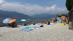 A pebbled beach with umbrellas and people sunbathing. - Villa Giulia apartment Vista Verde 5 min from the lake and town (Porto Valtravaglia)