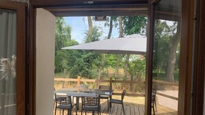 An outdoor wooden deck with a table and chairs, a large umbrella, and a view of a wooded area. - "p'tite maison" located 5 min from center parc Normandie (Mandres)