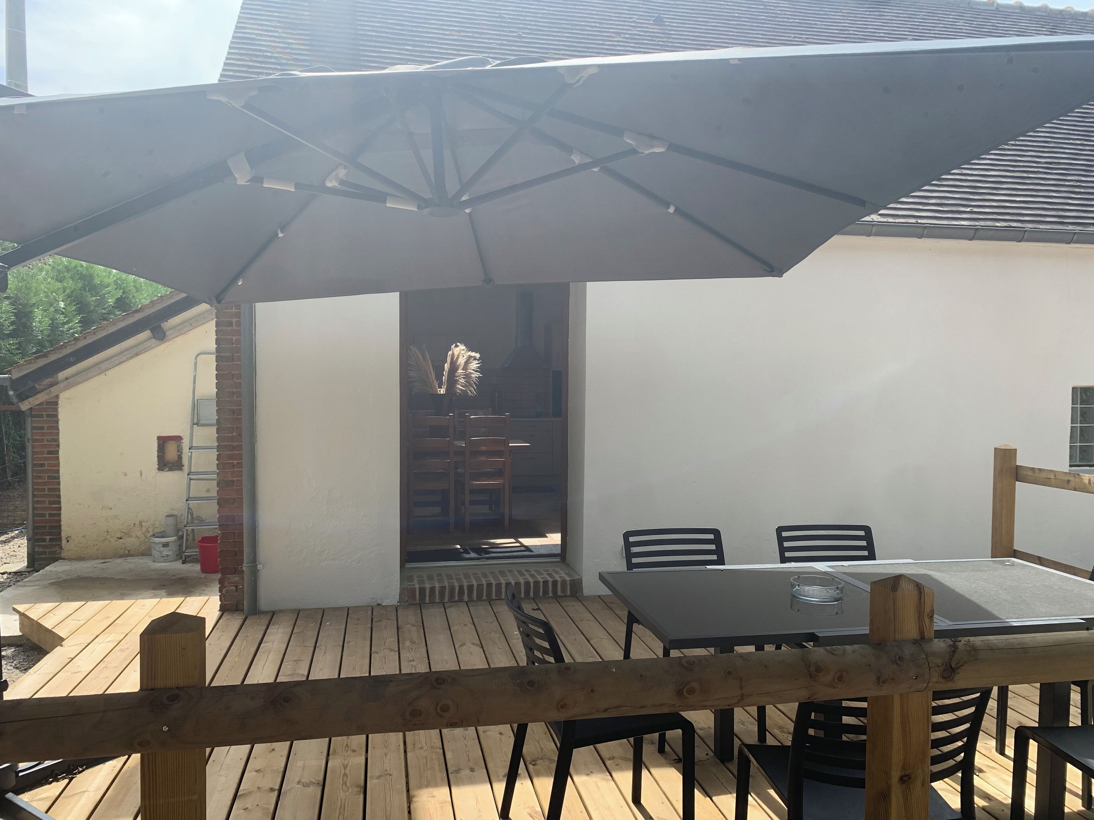 Une terrasse extérieure avec une table et des chaises, une clôture en bois et un espace abrité avec un toit.