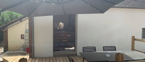 Une terrasse extérieure avec une table et des chaises, une clôture en bois et un espace abrité avec un toit.