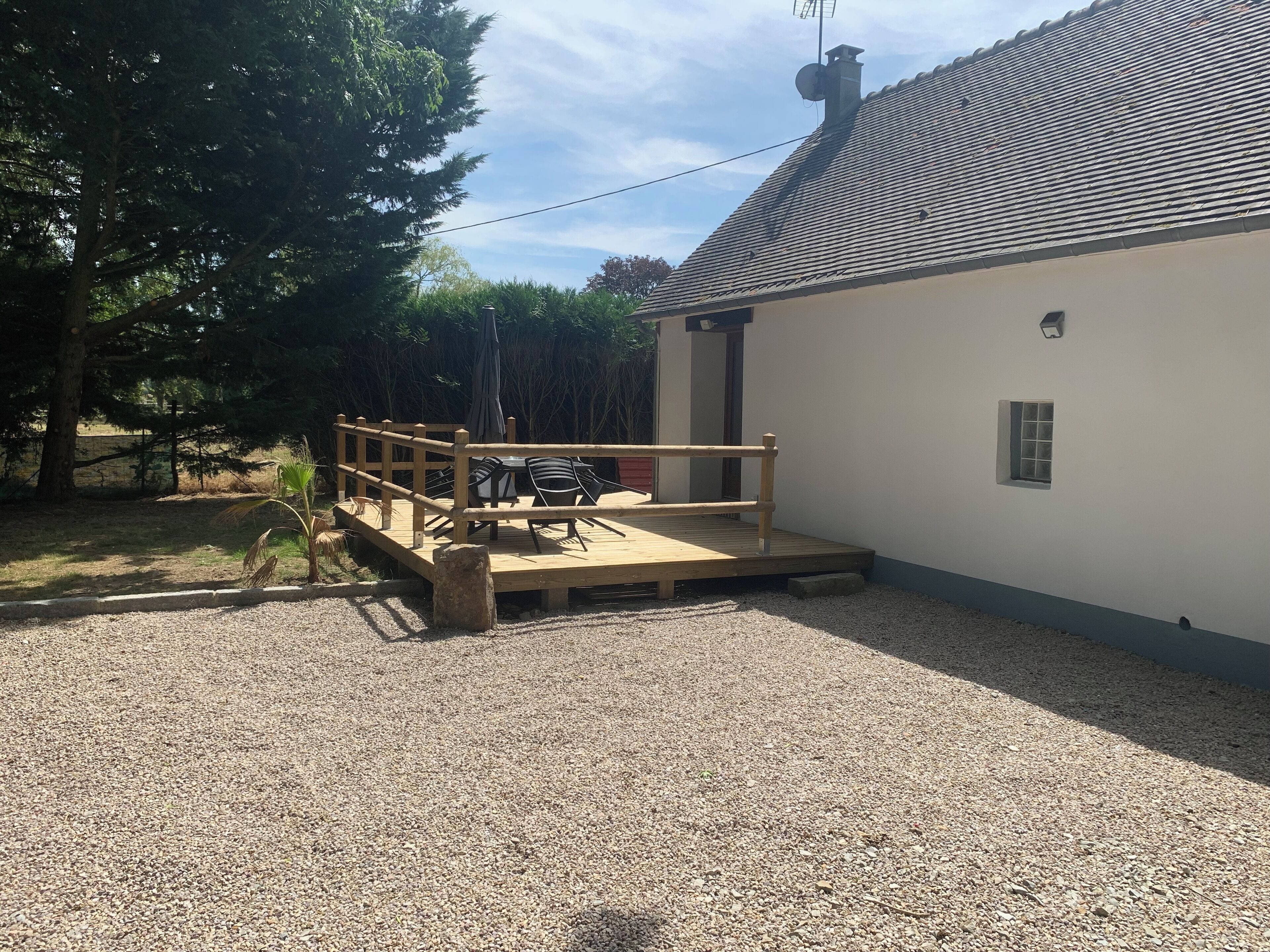Une terrasse en bois avec une table et des chaises, une petite fenêtre et un sol recouvert de gravier.