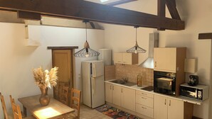 A compact kitchen with a dining area, featuring a wooden table, chairs, a refrigerator, a stove, and pendant lights. - "p'tite maison" located 5 min from center parc Normandie (Mandres)