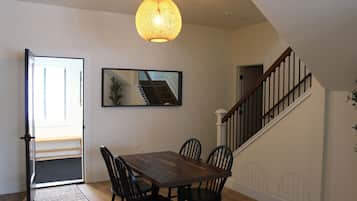 A dining area with a wooden table and chairs, a hanging light fixture, and a staircase with a railing.