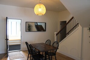 Un comedor con una mesa y sillas de madera, una lámpara colgante y una escalera con barandilla.
