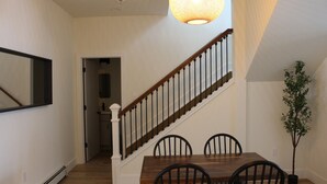 A dining area with a wooden table and chairs, a staircase with a railing, and a hanging light fixture. - Spacious 5 BR House on the River (Indian River)