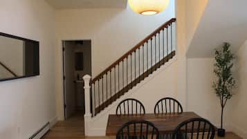 Un coin repas avec une table et des chaises en bois, un escalier avec une rampe et un luminaire suspendu.