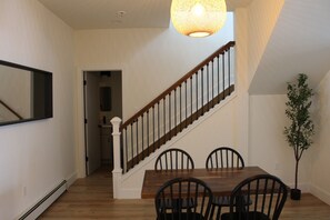 Ein Essbereich mit Holztisch und -stühlen, einer Treppe mit Geländer und einer Hängeleuchte.