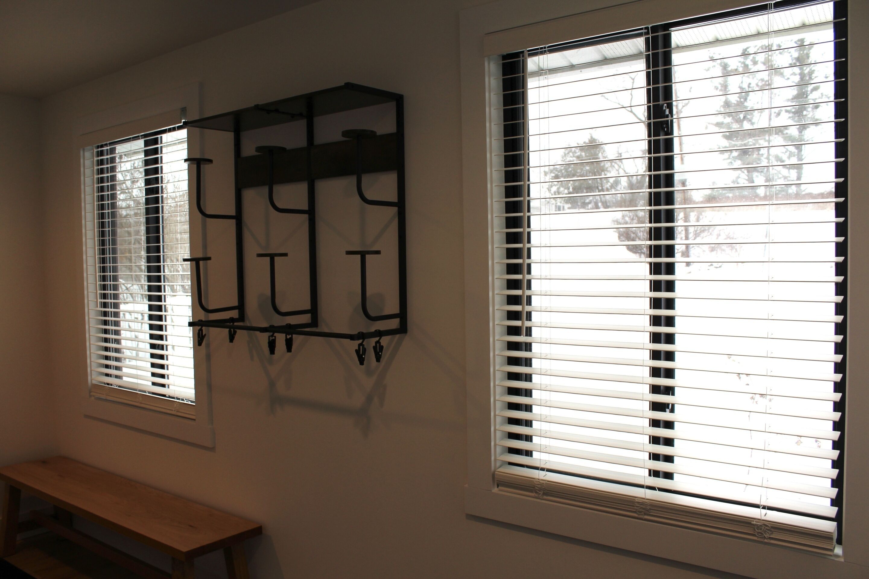 Two windows with blinds, a wooden bench, and a wall-mounted rack.
