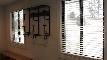 Two windows with blinds, a wooden bench, and a wall-mounted rack.