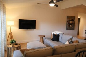 Un salon comprenant un canapé, un pouf, une lampe et un téléviseur fixé au mur.