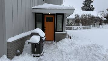 Une maison d’habitation dont la porte d’entrée est recouverte de neige, et devant laquelle se trouve une souffleuse à neige.
