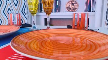 A dining table with orange plates and clear glasses, a patterned wall, and bookshelves with books and a New York City-themed plate.