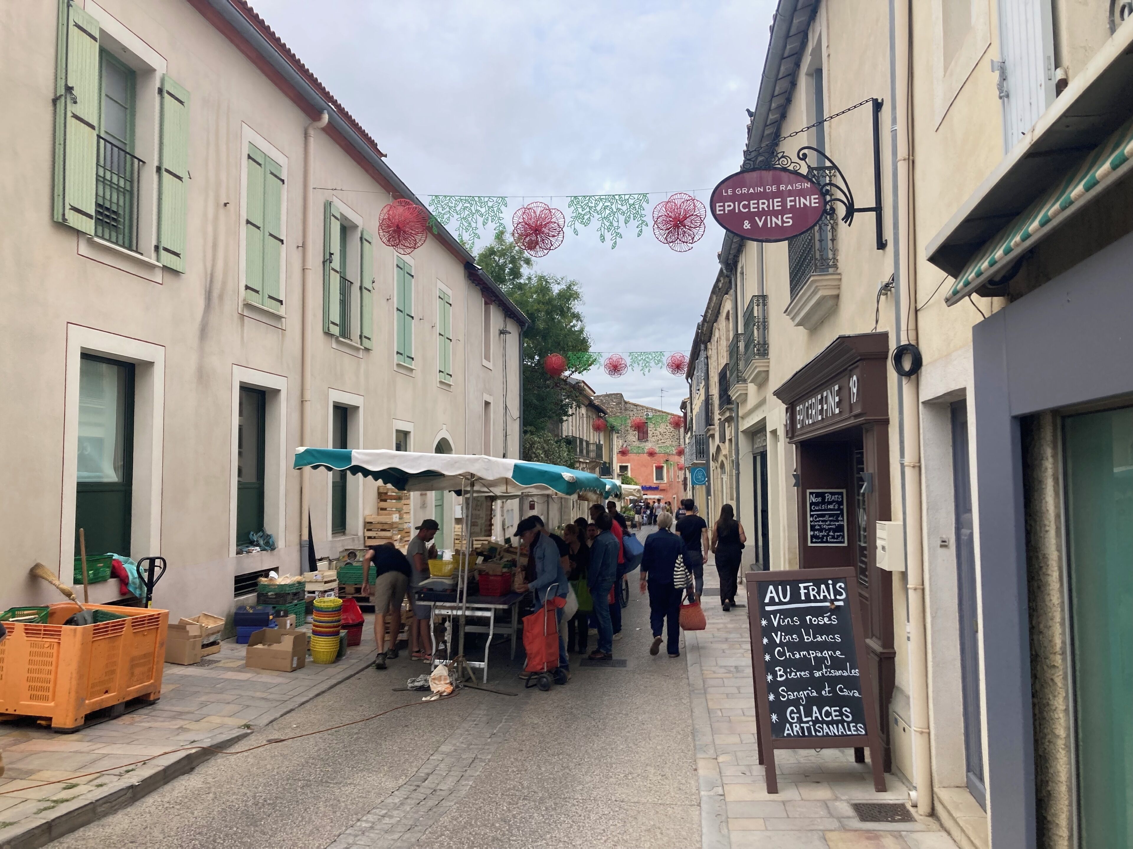 A narrow street with a market stall and a signboard listing wine and champagne.