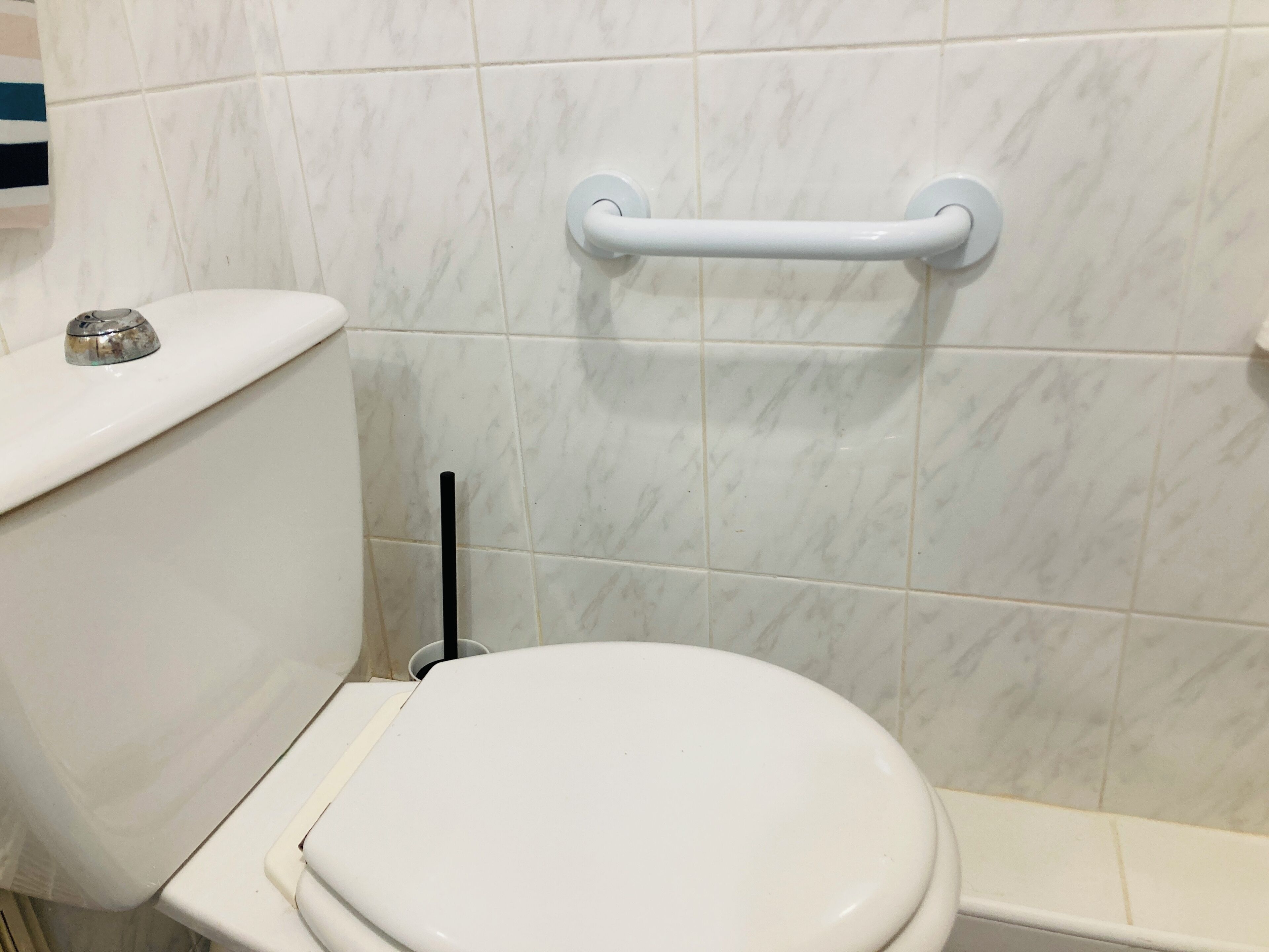 Et badeværelse med toilet, gelænder og væg beklædt med marmor.