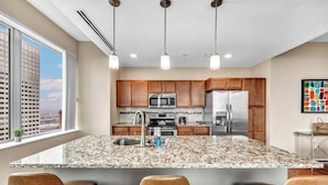 Une cuisine moderne dotée de plans de travail en granit, d’appareils électroménagers en acier inoxydable, d’armoires en bois et de luminaires suspendus.