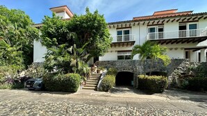Um edifício de dois andares com fachada de pedra, uma varanda e uma escadaria que leva à entrada.