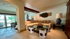 Uma sala de estar com mesa de centro de vidro, sofá bege e um espaço de jantar com cadeiras e mesa.