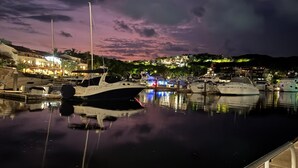 Um porto ao anoitecer, com barcos atracados, refletindo as luzes de edifícios próximos.