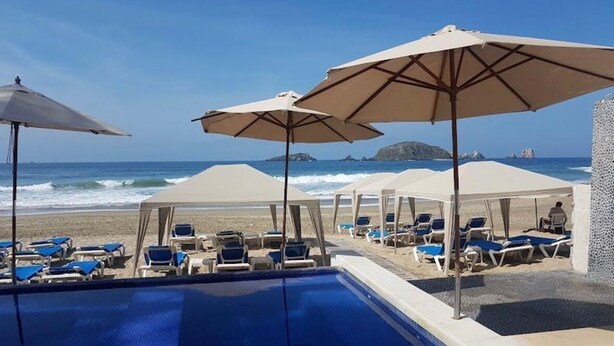Área à beira da piscina com espreguiçadeiras e guarda-sóis, com vista para o mar.