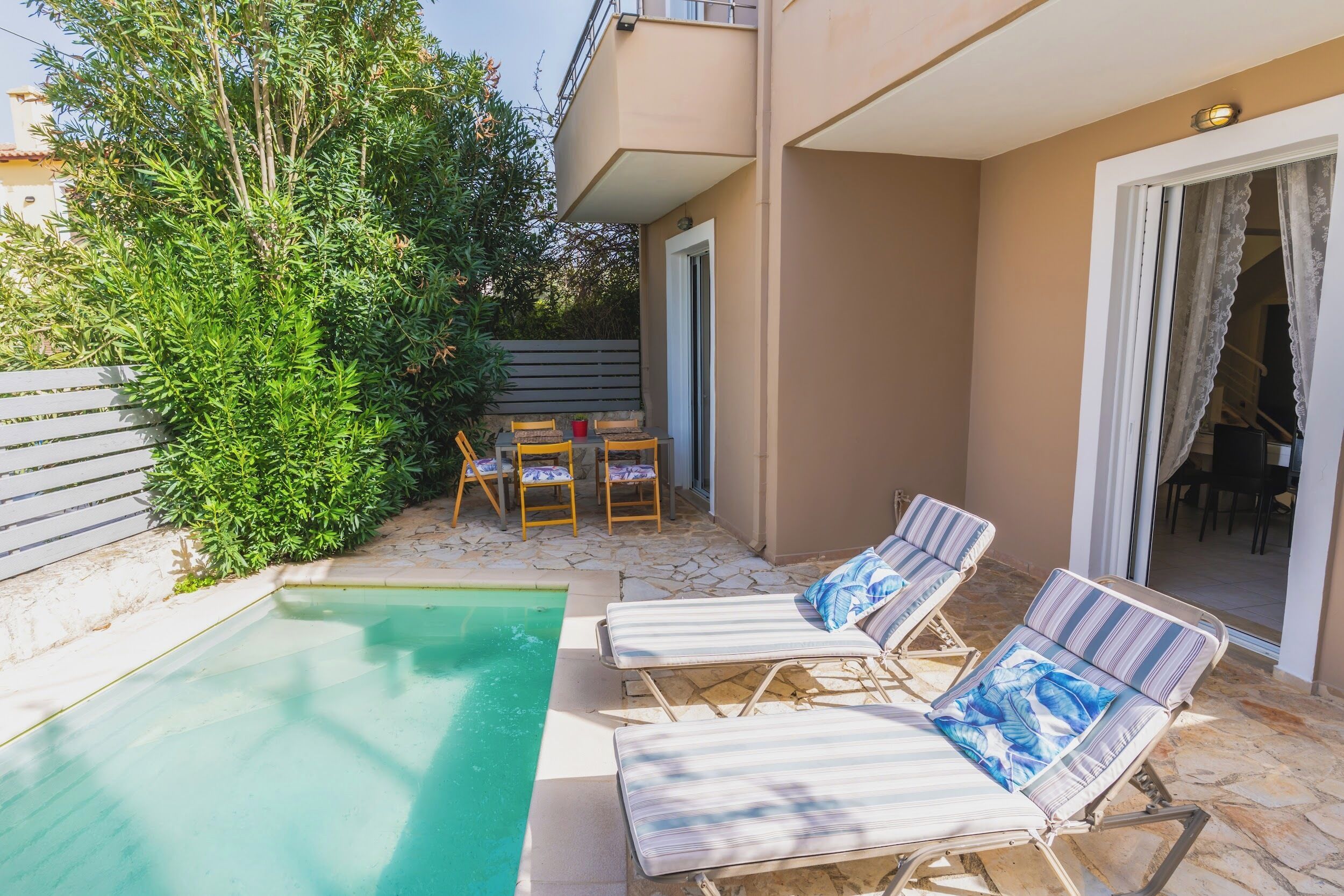 Ein Poolbereich mit Liegestühlen und einem Tisch, umgeben von Grünpflanzen und einem Gebäude mit Balkon.