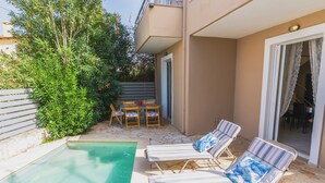 Ein Poolbereich mit Liegestühlen und einem Tisch, umgeben von Grünpflanzen und einem Gebäude mit Balkon.