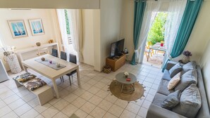 Een goed verlichte woonkamer met een eethoek, een bank, een televisie en uitzicht op de omgeving.