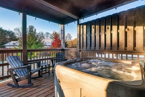 Un bain à remous sur une terrasse en bois, avec des chaises, donnant sur une étendue d’eau et des arbres.