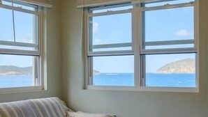 A room with a sofa, a wicker coffee table, and large windows offering a view of the sea. - Serene Escape + 3 Mins to Beach + Dining (St. Thomas)