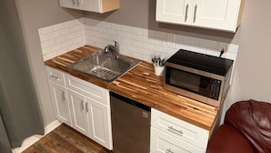 Una cucina compatta con pensili bianchi, un lavello in acciaio inossidabile, un forno a microonde e un piano di lavoro in legno.