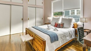 Ein Schlafzimmer mit einem hölzernen Bett, einer Sitzbank, einem Schreibtisch und einem Fenster mit Jalousien.