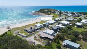 Vue aérienne d’un quartier résidentiel situé sur la côte, avec des maisons modernes, une plage et l’océan.