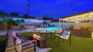 Un patio trasero con piscina, mobiliario exterior y zona de bar.