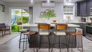 Una cocina moderna con una isla central, taburetes de bar, iluminación colgante y armarios oscuros.