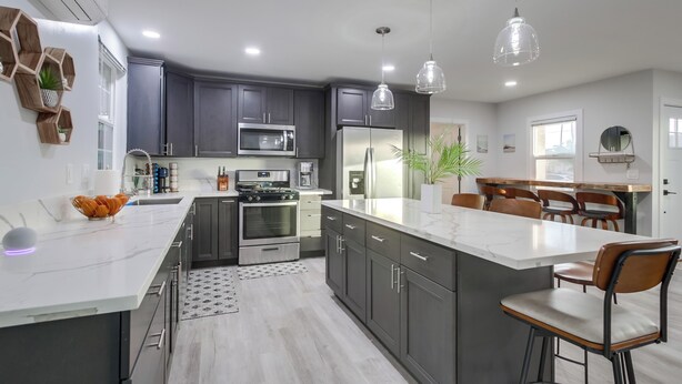 Una cocina moderna con armarios oscuros, electrodomésticos de acero inoxidable, encimera de mármol e iluminación colgante.