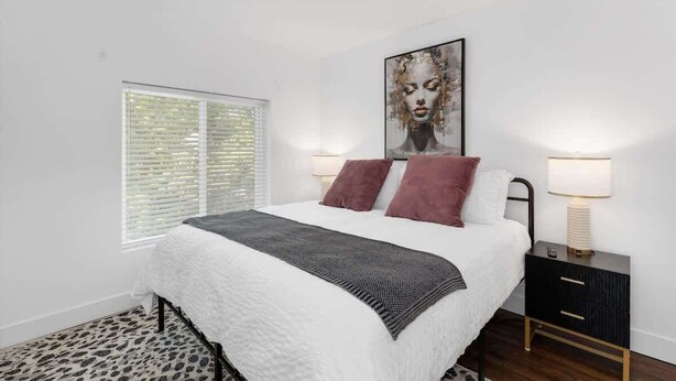 A bedroom with a bed, two bedside lamps, a nightstand, a window with blinds, and a wall-mounted artwork. - 5BR Detroit near Downtown • 3 King Beds Sleeps 14 (Detroit)