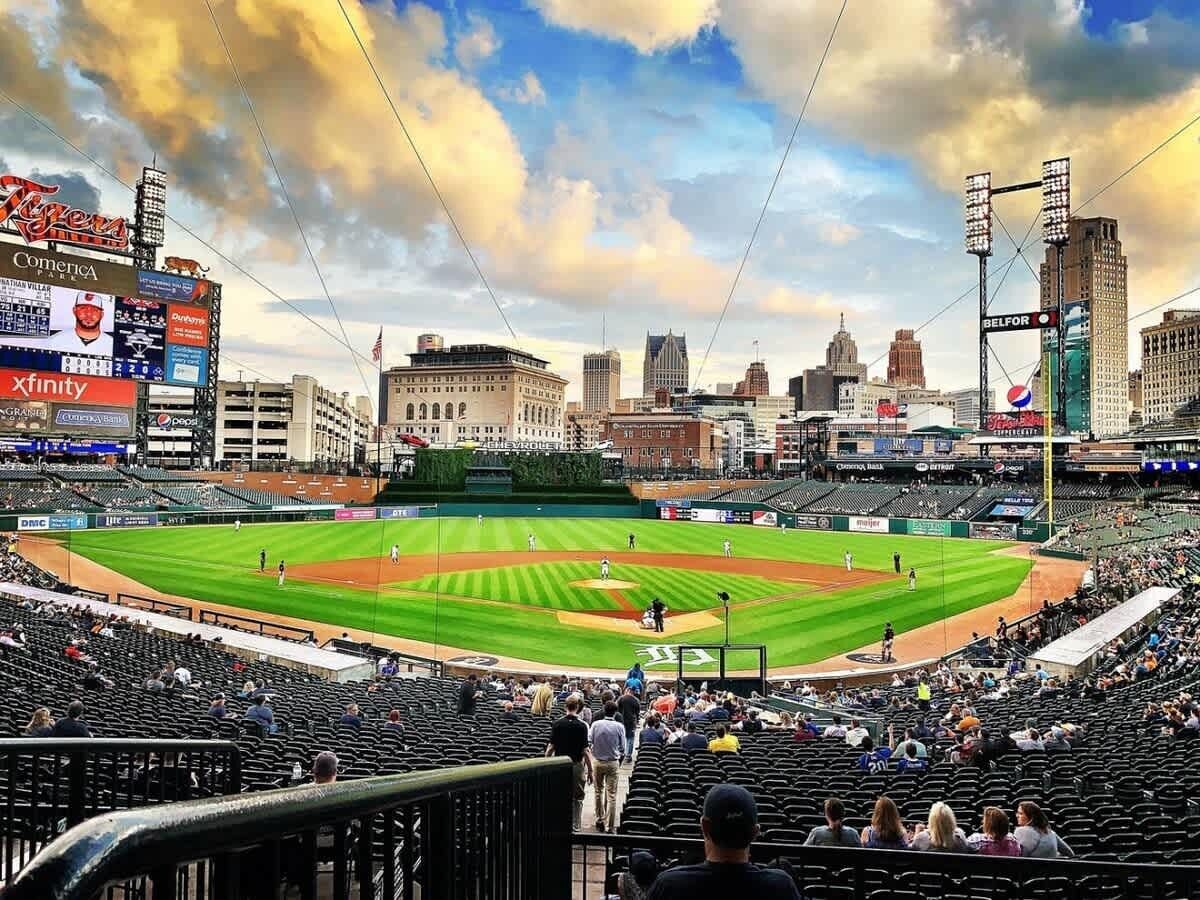 Un estadio de béisbol con un amplio campo de juego, zonas de asientos y un horizonte urbano al fondo.