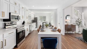 A modern kitchen with white cabinetry, a central island, and a dining area with a long table. - 5BR Detroit near Downtown • 3 King Beds Sleeps 14 (Detroit)